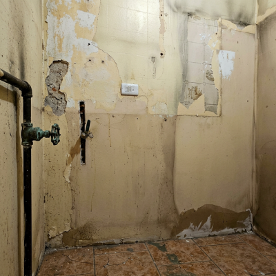 Fotografía de una pared de cocina con pintura amarilla dañada y restos de azulejos antes de la instalación de wallpanel.