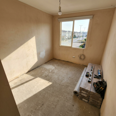 Dormitorio vacío con suelo de concreto desnudo antes de la instalación de piso flotante.